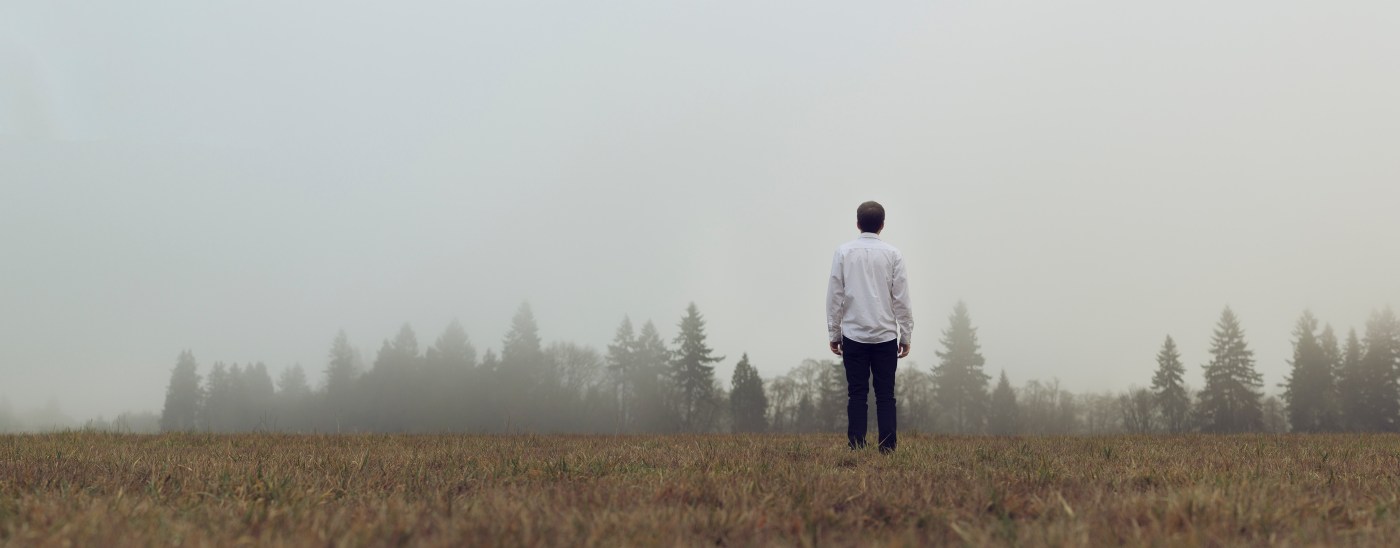 Man alone looking across field at trees in foggy distance.